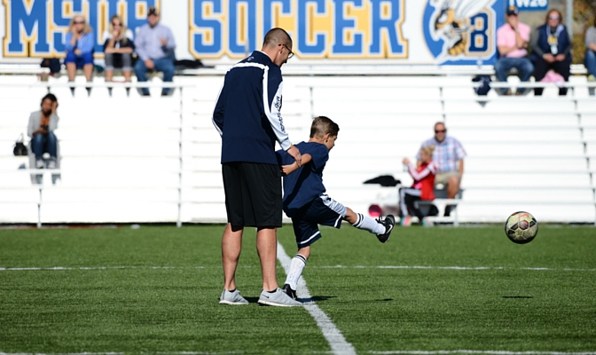 Montana State Billings head men's soccer coach Alex Balog with seven-year old Sebastien Easton, taking the team's ceremonial kick-off for the MSUB Kicks Cancer match.